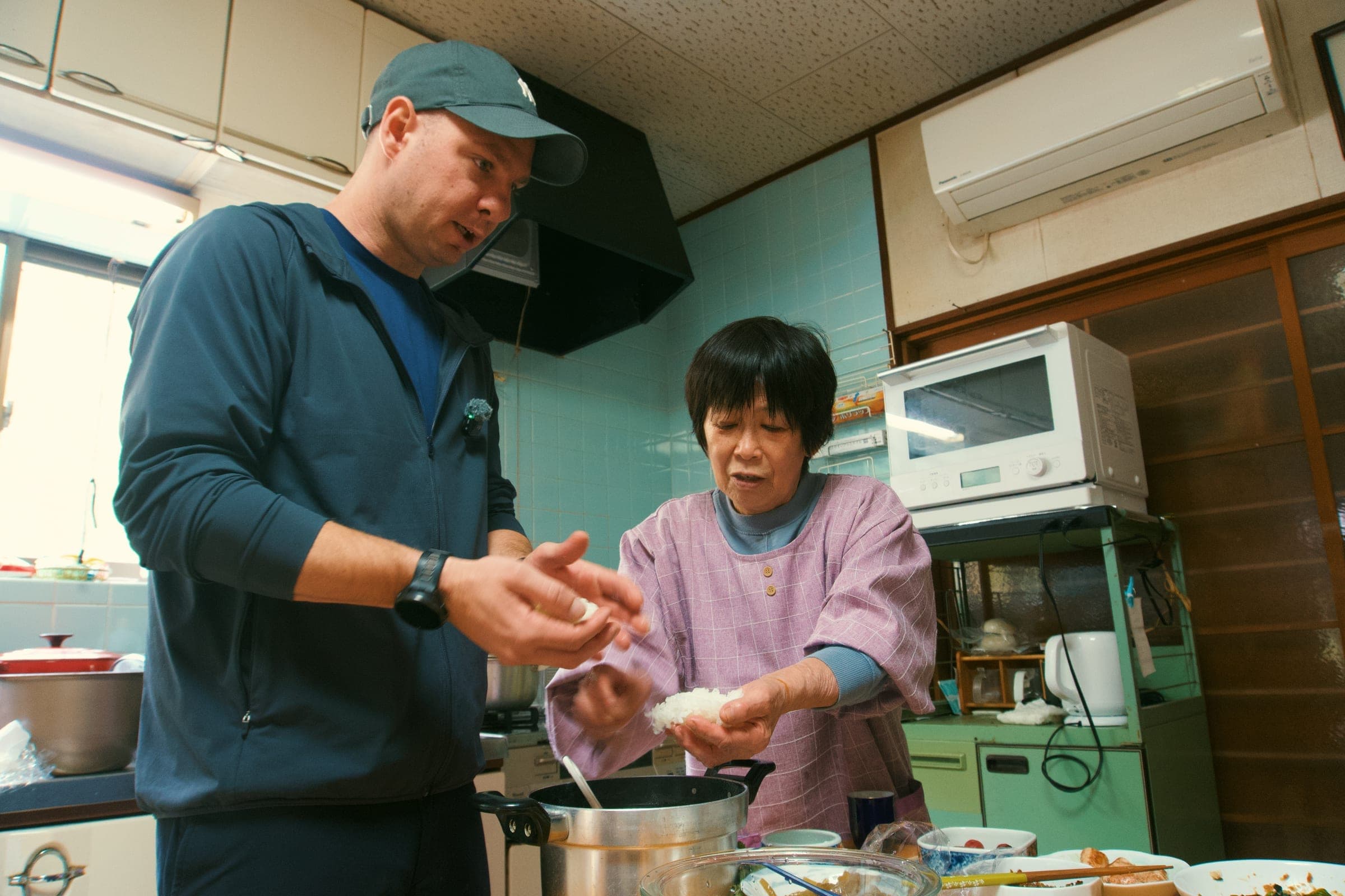 Harita-san pressing onigiri in her kitchen while Jason cooks beside her